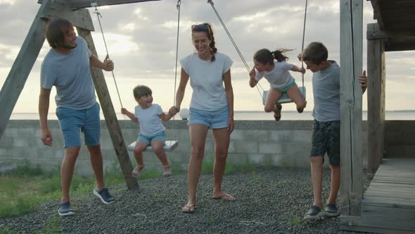 Happy Family Rolls Young Children on a Swing Outdoors at Sunset