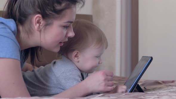 Modern Family Leisure, Nice Infant Boy with Young Mum Have Fun with Touch Tablet Lying on Bed at