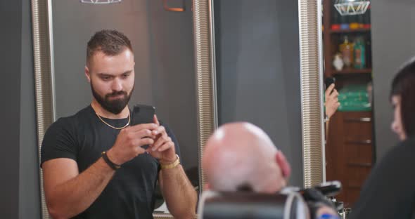 Young Bearded Man in Front of the Wall in Black Tshirt with Smartphone in Hands Records Video of