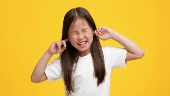 Naughty Little Asian Girl Plugging Ears With Fingers Yellow Background