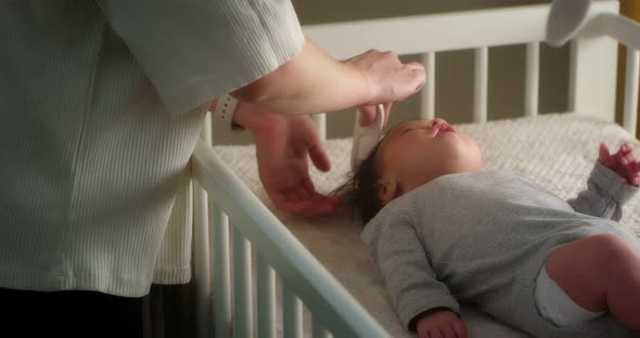 Loving Mother is Combing a Newborn Baby Lying on Her Back in Child Crib