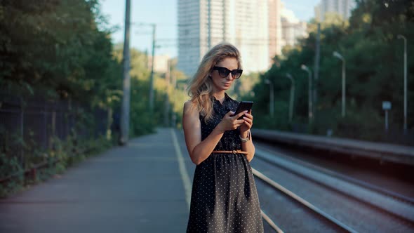 Woman Holding Mobile Phone And Waiting Public Transport On Train Station. Woman Waiting Train.