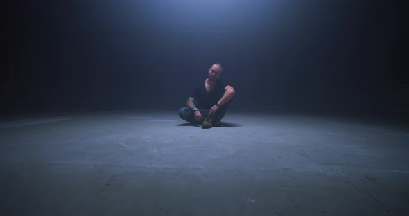 Tattooed Man Sitting in Dark Room