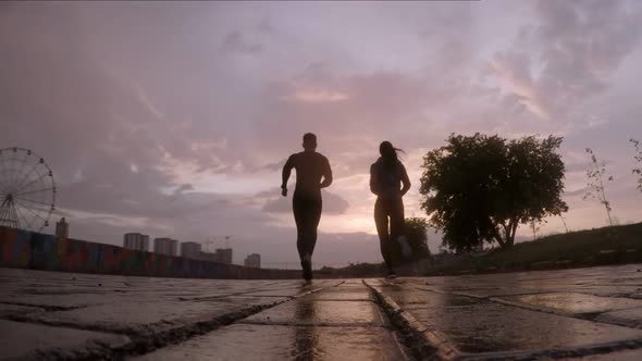 Woman and Man Running on Wet Asphalt at Sunset