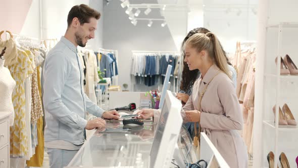 Female Customers Paying with Smartphone Talking to Salesman and Taking Shopping Bags