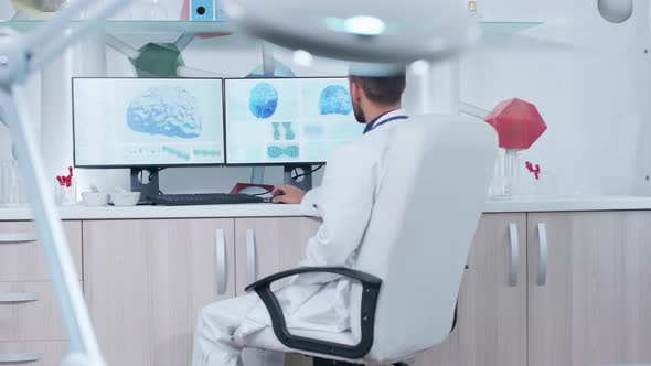 Doctor Working in Modern Research Facility with 3D Brain Scans Showing on Monitors