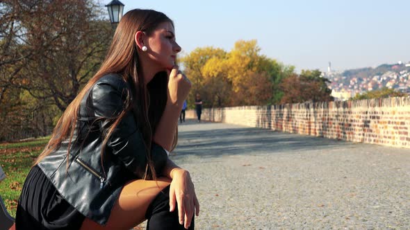 Young Beautiful Woman Sits on the Bench in Autumn Park and Relax (Looks Around)