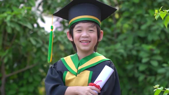 Happy Asian Child In Graduation Gowns Holding A Certificate