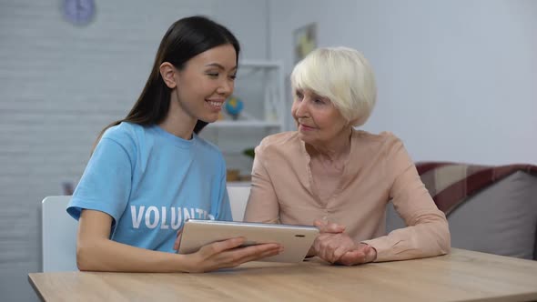 Social Carer Showing Tablet Application to Senior Female Pensioner, Support