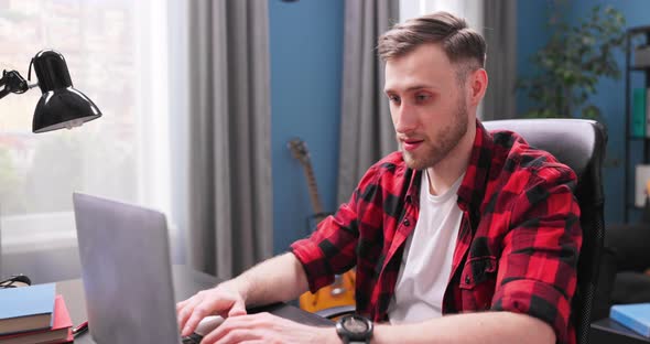 A Handsome College Student Boy is Studying Remotely While Sitting at a Desk in Living