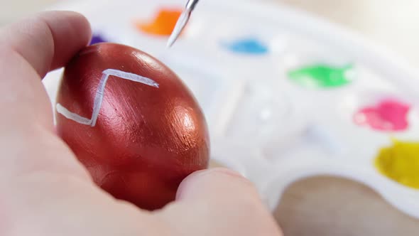 Happy Easter Close Up. A white man drawing white lines with a brush on a copper coloured Easter egg