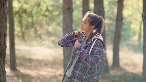 Woman Hipster Traveler Puts on Small Backpack in Autumn Forest