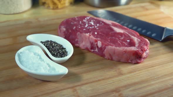 Rib Eye Steak Being Seasoned on a Chopping Board
