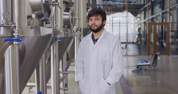 Portrait of Young Man Technologist in Lab Coat Posing at Camera in Brewery Plant