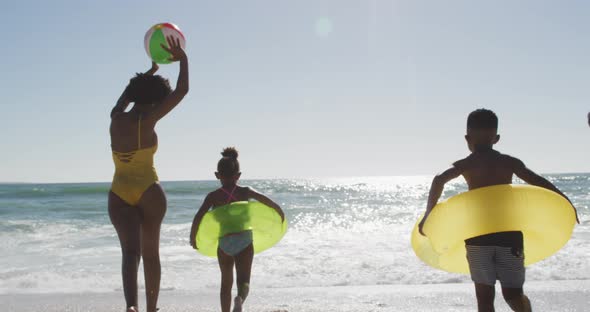 African american family with inflatables running into water on sunny beach