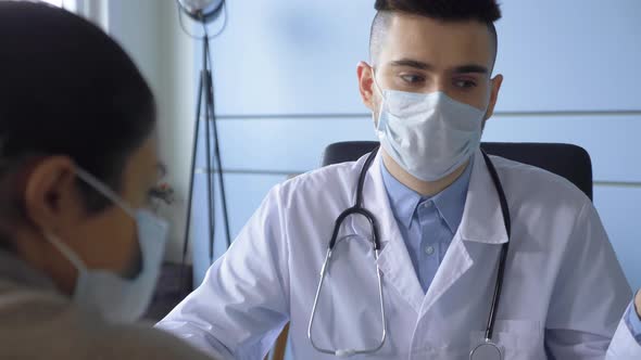 A Young Male Doctor in a Mask Talks to an Indian Patient Shows The Result of A Disease Test