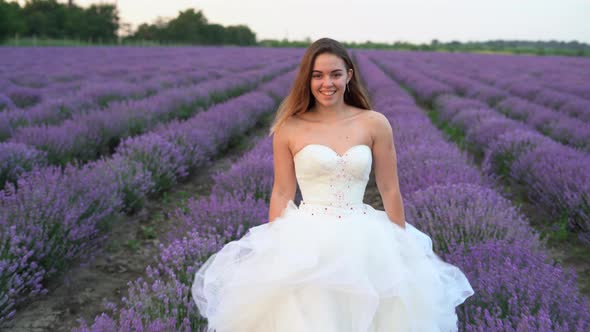 A Young Beautiful Caucasian Woman in a White Wedding Dress is Walking Along the Lavender Fields