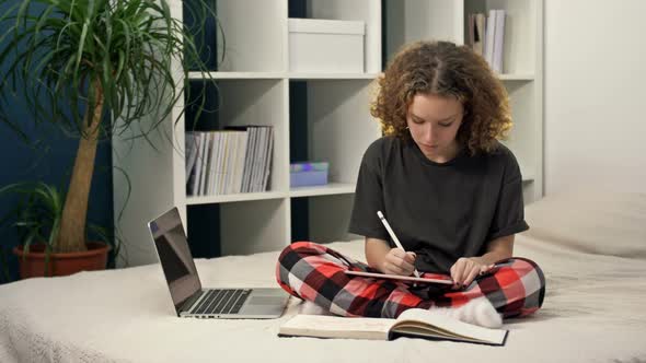 Cute Teenage Girl Doing Homework Sitting on the Bed at Home