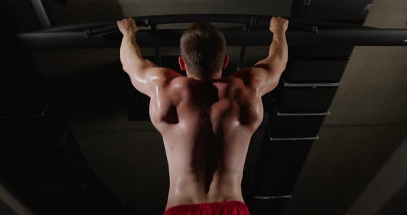 A man with beautiful muscles on his back, in the gym, pulls himself up on a horizontal bar