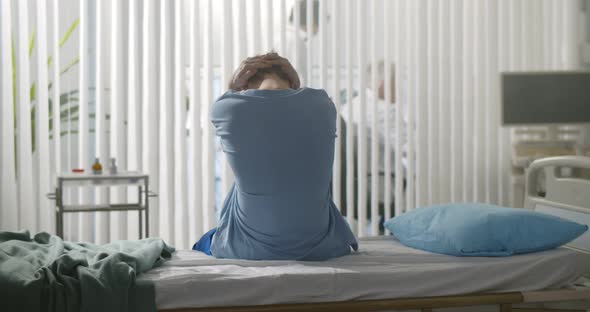 Back View of Young Desperate Man Sitting at Hospital Bed Alone