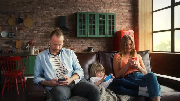 Young Pair and Their Child Boy are Smiling Using Smartphones While Sitting on Sofa in Studio