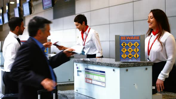 Two female airport staff checking passport and interacting with commuter at check-in desk
