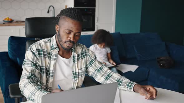 Close Up of Busy African American Man Working with Laptop and Documents at Home Office His Little