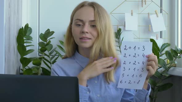 Young Female Teacher Sitting at Desk and Using Laptop Teaching Mathematics at Home