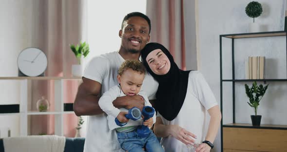 African Man and Muslim Woman and their Dark-Skinned Small Child which Looking at Camera at Home