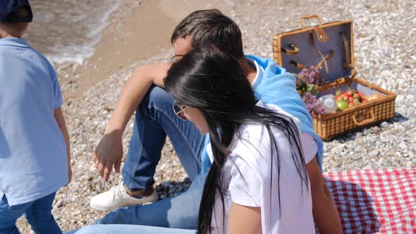 Family picnic with boy and girl near sea on sunny summer day. Basket with water, fruit and croissant