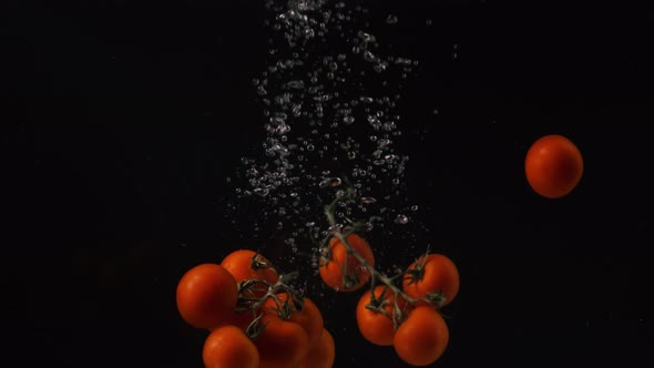 Red Cherry Tomatoes with Water Droplets Collide on Black Background. Vegetables Falling Into Water