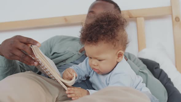 Man and Toddler Reading Book in Bed