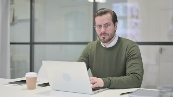 Young Businessman Showing Thumbs Down Sign While Using Laptop in Office