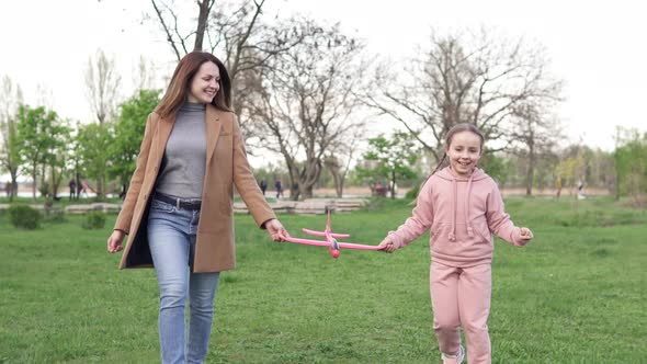 Happy mom and teen daughter having fun outdoors, carefree family playing with red airplane toy model