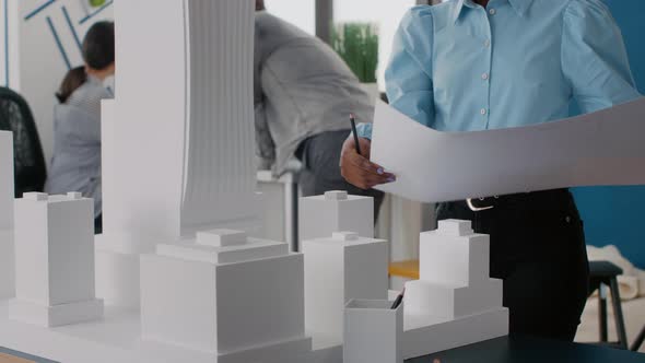 Close Up of Architect Holding Blueprints Plan and Looking at Building Model for Urban Project