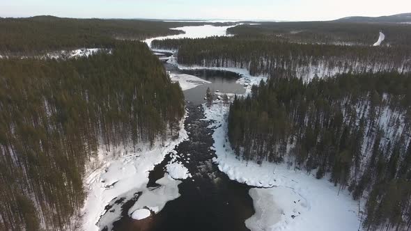 Flight over a frozen river and winter snowy forest