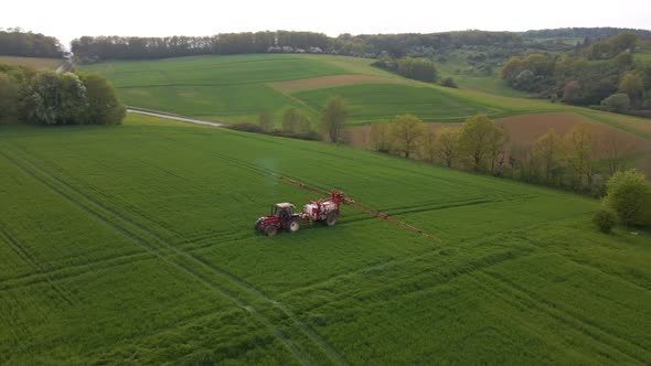 aerial footage of a tractor driving its sprinkler system unfolded in a huge green meadow to spray it