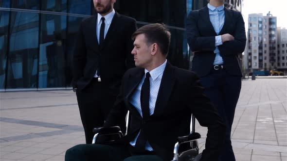 Epic Shot of Invalid Male with Disabled Legs Sitting on Wheelchair with His Colleagues