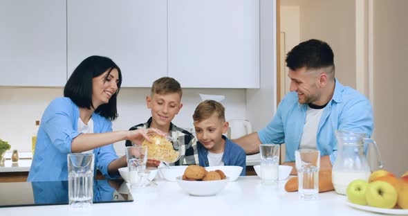 Mother Putting Into Bowl Corn Flakes Cereal to Her Two Sons while Having Breakfast