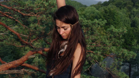 Woman in a Blue Silk Dress Forging By a Pine Tree Hugging Herself As She Does so