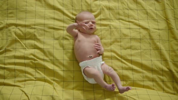 FULL SHOT TOP DOWN - Newborn baby on yellow bedsheets looking at the camera