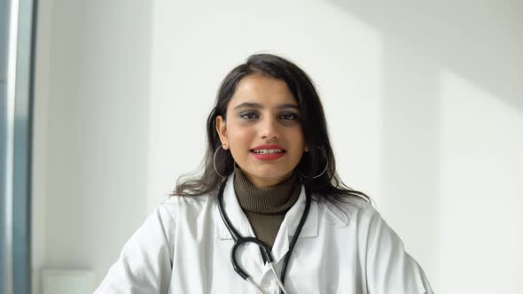 Indian Female Doctor in a White Coat with a Stethoscope Communicates with the Viewer Directly Into