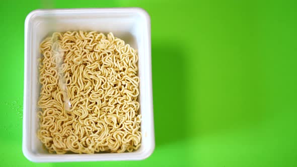 Close Up of Instant Noodles on Green Background. Boiling Water Is Poured Into Plate with Macaroni.