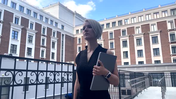 A Business Lady with a Tablet Walks Against the Backdrop of a Red Brick Building