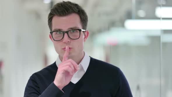 Serious Young Businessman Putting Finger on Lips 