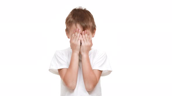 Smiling Elmentaryschool Aged Boy Closing Eyes with Hands and Laughing Standing on White Background