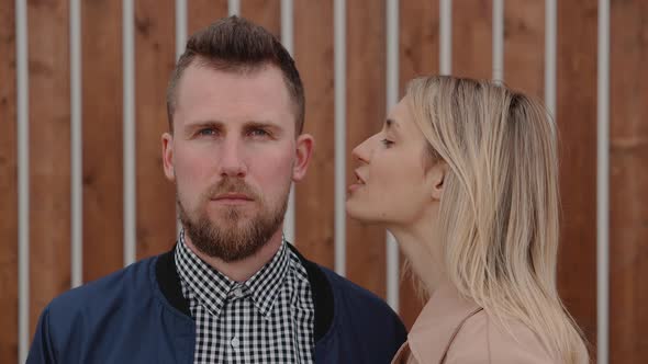 Pretty Blonde Woman Is Whispering on Ear of Handsome Bearded Man Outdoors