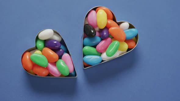 Video of overhead view of multi coloured sweets in two heart shapes over blue background