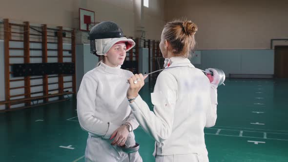 Two Young Women Fencers in White Protective Suits Standing on Front of Each Other and Having