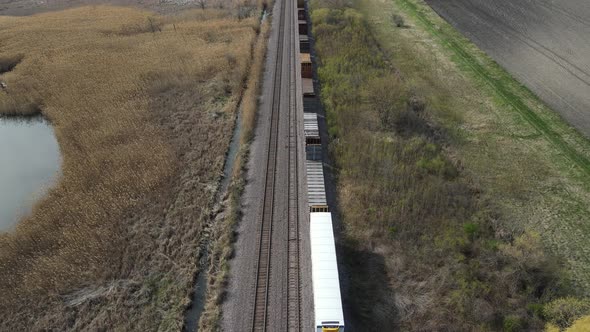 Train waiting on tracks in autumn with farm land on both sides along with water drainage.